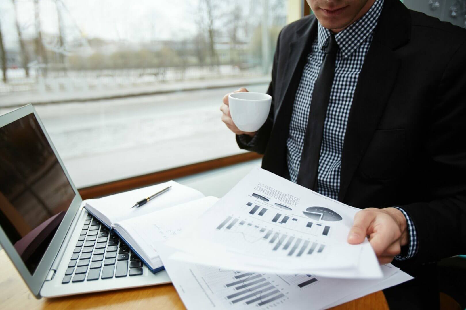 Businessman reviewing financial charts at a laptop by a window